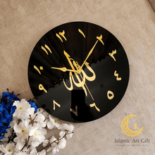 Load image into Gallery viewer, Black wall clock with gold Arabic calligraphy on a beige surface with flowers.